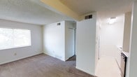This single-floor residential space offers a clean and functional layout with a neutral color palette throughout. The interior is finished with soft, wall-to-wall carpeting that adds warmth underfoot, complemented by crisp white walls and classic white baseboards that lend a bright, tidy aesthetic to each room. The textured popcorn ceiling is consistent throughout, giving the space a familiar and understated character. A built-in closet with sliding doors provides practical storage, making efficient use of the available space. HVAC vents are integrated into both the walls and ceiling, ensuring climate control throughout the unit. Natural light filters in through a window, contributing to a light and airy feel despite the modest scale. The layout flows in a straightforward manner, with a corridor connecting the various areas of the home. Overall, this space presents a simple, move-in-ready interior that offers a solid foundation for personalization, with all the essential features needed for comfortable, everyday living on a single level.