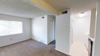 This single-floor residential space offers a clean and functional layout with a neutral color palette throughout. The interior is finished with soft, wall-to-wall carpeting that adds warmth underfoot, complemented by crisp white walls and classic white baseboards that lend a bright, tidy aesthetic to each room. The textured popcorn ceiling is consistent throughout, giving the space a familiar and understated character. A built-in closet with sliding doors provides practical storage, making efficient use of the available space. HVAC vents are integrated into both the walls and ceiling, ensuring climate control throughout the unit. Natural light filters in through a window, contributing to a light and airy feel despite the modest scale. The layout flows in a straightforward manner, with a corridor connecting the various areas of the home. Overall, this space presents a simple, move-in-ready interior that offers a solid foundation for personalization, with all the essential features needed for comfortable, everyday living on a single level.
