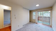 This single-floor unit offers a practical and efficient layout across three bedrooms, one bathroom, and a combined kitchen and living area. The living room features neutral carpet flooring, a ceiling fan with integrated lighting, a textured ceiling, and a small window with a roller shade, providing a modest yet functional gathering space that connects openly to adjacent rooms.

The galley-style kitchen is equipped with warm-toned wood cabinetry, granite-look countertops, a white electric range with overhead ventilation, and a built-in sink. Light hardwood flooring runs throughout the kitchen and extends into the hallway, contributing a consistent, clean aesthetic. A window at the end of the kitchen allows natural light to filter through.

The bedrooms are carpeted and present a clean, neutral palette. Two bedrooms feature sliding glass doors opening directly onto a wood-railed outdoor deck with views of surrounding greenery, offering notable natural light and outdoor connectivity. Sliding panel closets provide storage within these rooms.

The bathroom includes a wood-framed medicine cabinet mirror, a granite-look vanity with warm wood cabinetry, hardwood flooring, a Hollywood-style light bar, and a tiled shower enclosure, rounding out this efficiently designed unit.