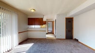 Located at 1690 Dominion Dr in Akron, Ohio, this single-floor unit offers a straightforward, functional layout with several distinct living spaces connected in an efficient flow. The living area is generously sized, featuring neutral gray carpeting, warm wood baseboards, and a large sliding glass door fitted with vertical blinds that floods the room with natural light and provides a view of the outdoors. A wall-mounted air conditioning unit serves the space, and an interior door leads to additional rooms.

The galley-style kitchen is positioned adjacent to the living area and features rich, dark reddish-brown wood cabinetry both above and below the counter. A single-basin sink, a white range with overhead ventilation, and a refrigerator are included. The kitchen benefits from a window that brings in natural light, and the flooring transitions to a durable vinyl surface.

The bedroom is a well-proportioned room with soft carpeting and two windows overlooking greenery outside, allowing ample daylight to enter from multiple directions.

The bathroom includes a vanity with an integrated sink and storage cabinet below, a mirrored medicine cabinet above, a toilet, and a shower area. The floor features classic vinyl tile, and a floor vent provides climate control. Wood-toned trim accents tie the bathroom's finishes together.
