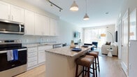 This thoughtfully designed single-floor residence offers a cohesive open-concept layout that seamlessly connects the kitchen, dining, and living areas. The kitchen is a standout feature, appointed with crisp white shaker cabinetry, granite countertops, and a full suite of stainless steel appliances including a refrigerator, range, microwave, and dishwasher. A central island with bar seating provides additional prep space and a natural gathering point, while pendant lighting and track lighting enhance both function and ambiance. Light hardwood flooring runs throughout the main living areas, lending warmth and continuity to the space. The living room is bright and welcoming, with large windows and a sliding glass door that invite an abundance of natural light and offer views of the surrounding greenery. Two well-proportioned bedrooms each feature large windows with outdoor views and ample natural light, creating restful and comfortable retreats. The bathroom is finished with granite-topped white vanity cabinetry, large-format tile flooring, and a full tub and shower combination with white subway tile surround. Neutral warm tones and a clean, contemporary aesthetic are carried throughout the entire residence, creating a cohesive and inviting atmosphere.