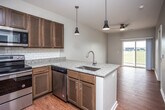 This single-floor residence is designed with an open-concept layout that seamlessly connects the kitchen and living areas, creating a spacious and functional flow. The kitchen is a standout feature, equipped with rich dark wood cabinetry, granite countertops, a white subway tile backsplash, and a full suite of stainless steel appliances, including a refrigerator, range, microwave, and dishwasher. A peninsula with an undermount sink extends into the living space, illuminated by a pair of modern pendant lights that add a contemporary touch. Warm hardwood-style flooring runs throughout the main living areas, complementing the neutral wall tones. The living area is fitted with a ceiling fan and receives natural light through a sliding glass door that opens to the outdoors. A separate room features a wide window with outdoor views of open green space, offering a bright and airy atmosphere. A bathroom with hardwood-style flooring is conveniently situated adjacent to a dedicated laundry area with a stacked washer and dryer unit. The overall ambiance of the space is clean, modern, and well-appointed, with consistent finishes tying each area together cohesively.