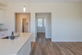 This single-floor residence presents a clean, contemporary design characterized by an open and functional layout. The kitchen serves as the centerpiece of the living area, featuring white shaker-style cabinetry extending to the ceiling, light-toned countertops, and a full suite of stainless steel appliances including a French door refrigerator, gas range, and built-in microwave. A generously sized central island with an integrated sink and pendant lighting above provides both additional workspace and a natural gathering point. Light hardwood flooring flows throughout the main living areas, lending warmth and continuity to the space.

The bedrooms are carpeted in a neutral tan tone and benefit from multiple windows, allowing ample natural light and outdoor views of surrounding greenery. The room proportions are comfortable, with clean white trim and panel-style doors adding a polished finish. A programmable thermostat is conveniently situated in the hallway for easy climate control.

The bathroom is bright and practical, featuring hardwood-style flooring, a tub with shower, a tall storage cabinet, and a window that introduces natural light. Throughout the residence, a neutral warm palette, recessed lighting, and consistent finishes create a cohesive, move-in-ready ambiance.