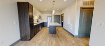 This contemporary apartment boasts a well-designed floor plan that maximizes space and functionality. The heart of the home is a stunning kitchen with two-tone cabinetry, quartz countertops, and stainless steel appliances. A large island with pendant lighting serves as both a prep area and casual dining space. The living area flows seamlessly from the kitchen, featuring wood-look flooring and a ceiling fan for comfort. The bedroom offers plush carpeting and windows for natural light. A modern bathroom and in-unit laundry add convenience. Throughout, the apartment showcases a neutral color palette with contrasting dark and light elements, creating a sophisticated and inviting atmosphere.