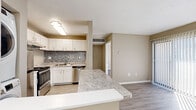 This single-floor unit offers a thoughtfully designed layout that blends functionality with modern finishes. The kitchen serves as the heart of the space, showcasing crisp white cabinetry, a decorative mosaic tile backsplash, granite countertops, and a full suite of stainless steel appliances including a range, dishwasher, and refrigerator. A peninsula counter extends into the open living area, providing additional prep space and a natural divide between the kitchen and the main living area. Light wood-look flooring runs throughout the common areas, contributing to a clean, contemporary feel. A standout convenience is the in-unit stacked washer and dryer, neatly tucked adjacent to the kitchen. The living area features a sliding door that allows natural light to filter in, creating a bright and welcoming atmosphere. The bedrooms are finished with soft carpeting and neutral-toned walls, offering a comfortable and versatile canvas. The bathroom is clean and functional, featuring a full soaking tub and shower combination with a simple, streamlined surround. Warm beige tones throughout the unit create a cohesive and inviting ambiance, making this a practical and move-in ready space.