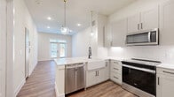 This thoughtfully designed two-story home in Austin, TX offers a clean, modern aesthetic with high-quality finishes throughout. The main floor features an open-concept kitchen and living area bathed in natural light, with warm wood-look flooring that flows seamlessly through the space. French doors in the living area open to the outdoors, enhancing the airy, connected feel of the lower level.

The kitchen is a standout, equipped with crisp white shaker cabinetry, quartz countertops, a farmhouse sink with a matte black faucet, and a full suite of stainless steel appliances including a refrigerator, range, microwave, and dishwasher. Globe pendant lights with brass accents add a contemporary touch overhead.

Upstairs, the generously sized primary bedroom features wood-look flooring, a ceiling fan, and dual windows that invite natural light and outdoor views. Two dedicated closets—including a walk-in with built-in shelving—provide excellent storage. An additional built-in shelving unit adds functional character to the bedroom area.

The two bathrooms are finished with crisp white tile, including a full bath upstairs showcasing marble-style wall tile surrounding a soaking tub. The overall palette of soft whites and warm neutrals creates a cohesive, inviting ambiance throughout this well-appointed Austin home.