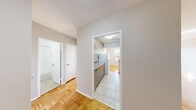 This 2-bedroom, 1-bathroom residence is thoughtfully laid out across a single floor, offering a functional and comfortable living arrangement. The interior is unified by warm parquet flooring throughout, lending a classic character to every room.

The living room is a bright and airy space, featuring a wide bank of windows that frame lush, tree-lined outdoor views and allow generous natural light to fill the room. A radiator runs beneath the windows, complementing the unit's heating system. The adjacent dining area connects seamlessly to the kitchen, which is outfitted with wood-toned cabinetry, speckled granite countertops, a white tile backsplash, and light tile flooring.

The primary bedroom is a well-proportioned room with a window offering urban views and a radiator beneath it. The second bedroom is similarly finished, with two doors providing access to a closet and the hallway. Both rooms continue the parquet flooring found throughout the residence.

A hallway connects the main living areas to the bathroom, which features a full bathtub with a handheld showerhead and clean white tile surround. The neutral color palette and clean finishes throughout create a bright, move-in-ready environment.