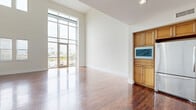 This multi-level loft in Carlsbad, CA offers a distinctive blend of industrial and residential design across three thoughtfully laid-out floors. The ground level features a spacious garage with polished concrete floors, exposed ductwork along the ceiling, and a frosted glass panel garage door that allows diffused natural light to filter in — ideal for use as a creative studio, workshop, or additional storage.

The main living floor is anchored by an open-concept kitchen and living area. The kitchen is outfitted with warm honey-toned cabinetry, granite countertops, a stainless steel double sink, and matching appliances. The living area is bathed in natural light from dramatic floor-to-ceiling windows that frame outdoor views, complemented by rich hardwood flooring throughout. A dedicated laundry room with overhead cabinetry and an electrical panel adds everyday convenience on this level.

The upper floor houses the generous primary bedroom, featuring gleaming hardwood floors, multiple windows with natural light, and access to a large walk-in closet with extensive shelving. Four full bathrooms are distributed across the floors, including one with accessibility features such as stainless steel grab bars and polished concrete flooring. Two staircases connect the levels, enhancing flow and functionality throughout this unique urban loft.