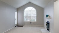 Located in Vancouver, WA, this single-floor, 3-bedroom, 2-bathroom home offers a well-organized layout with a functional mix of living spaces. The living room is an immediate standout, featuring soaring vaulted ceilings and a striking arched window that floods the room with natural light and provides views of the surrounding neighborhood. A secondary entry door with a sidelight panel adds convenient outdoor access. Neutral gray walls and plush carpeting carry throughout the living areas and bedrooms, creating a consistent, clean aesthetic.

The kitchen is open and efficiently designed, centered around an L-shaped peninsula with a breakfast bar overhang — ideal for casual dining. White cabinetry with gold-tone hardware, a stainless steel refrigerator, and a ceiling fan with light fixture complete the space, which features wood-look flooring that extends through the main traffic areas.

The hallway connects three carpeted bedrooms, including a generously sized primary bedroom with its own closet. The two bathrooms are finished with wood-look tile flooring, white vanities, and a full tub-shower combination. A dedicated laundry room houses a washer, dryer, and water heater. The home's straightforward, single-level layout makes it highly accessible and easy to navigate.