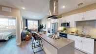 This thoughtfully designed 2-bedroom, 2-bathroom residence is laid out on a single floor, maximizing functionality and flow. The open-concept kitchen and living area serves as the heart of the home, where a large center island with granite-style countertops and a built-in gas cooktop anchors the space beneath a striking stainless steel island hood. White shaker cabinetry lines the kitchen walls, complemented by tile backsplash, under-cabinet lighting, and a full suite of stainless steel appliances including a refrigerator, microwave, and dishwasher. The living area extends naturally from the kitchen, bathed in natural light from large windows with outdoor views of the surrounding neighborhood. Light wood-style flooring runs throughout the main living spaces, adding warmth and continuity. Both bedrooms are comfortably proportioned, each featuring large windows with outdoor views and ceiling fans. The primary bedroom connects to a dedicated closet with built-in wire shelving. The two bathrooms are finished with granite-style vanity countertops, white cabinetry, large mirrors, and tub-shower combinations. Clean neutral wall tones and recessed lighting throughout lend the residence a modern, move-in-ready appeal.