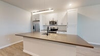 Located at 4665 Whitfield Ave in Sarasota, Florida, this modern single-story home showcases a clean, contemporary design with an open-concept layout and quality finishes throughout. The kitchen is a standout feature, centered around a large island with a quartz countertop, undermount sink, and matte black fixtures. White shaker-style cabinetry reaches toward the ceiling, complemented by a stylish elongated tile backsplash and a full suite of stainless steel appliances, including a French door refrigerator, electric range, and built-in microwave. Pendant lighting and recessed fixtures illuminate the space with a warm, modern glow. The kitchen flows naturally into the open living area, which features light-toned luxury vinyl plank flooring and a ceiling fan, creating a bright and airy atmosphere. Natural light enters through white-shuttered windows, adding to the home's fresh, neutral palette. The bedrooms are finished with plush wall-to-wall carpeting and ceiling fans, providing a comfortable and quiet retreat. The bathroom includes a soaking tub with full white tile surround, offering a clean and functional design. A dedicated laundry room with a full-size GE washer and dryer and built-in shelving adds everyday convenience to this well-appointed Sarasota home.