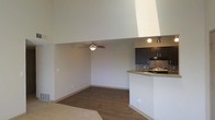 This single-floor residence showcases a thoughtfully designed open-concept layout that maximizes both space and functionality. The living area is immediately distinguished by its impressive vaulted ceilings, which lend an airy, expansive feel to the interior. Hardwood-style flooring in a warm, rich tone flows throughout, adding a touch of elegance and visual continuity to the space.

A ceiling fan with an integrated light fixture is centrally positioned in the living area, providing both comfort and ambient lighting. The neutral wall tones create a clean, versatile backdrop that complements a variety of design styles.

The kitchen is seamlessly integrated into the open floor plan via a raised breakfast bar counter, making it ideal for casual dining or entertaining. Dark espresso-toned cabinetry provides a striking contrast against the light countertops, while a tasteful tile backsplash adds texture and visual interest. Under-cabinet lighting and track lighting illuminate the workspace effectively. A gas range and built-in microwave round out the kitchen's practical amenities.

A subtle step-down in ceiling height between the kitchen and living areas creates a natural sense of zone definition without compromising the open feel. Overall, the space presents a clean, modern aesthetic with functional design details throughout.