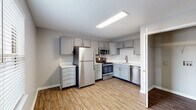 This single-floor residence in Louisville, KY offers a well-organized layout with a practical and cohesive design. The kitchen serves as a functional centerpiece, outfitted with gray shaker-style cabinetry, white countertops, and a full suite of stainless steel appliances including a refrigerator, range, microwave, and dishwasher. Wood-look plank flooring runs throughout the kitchen and main living areas, contributing a warm, clean aesthetic. The open connection between the kitchen and living area allows for an easy flow, with the living space receiving natural light through a window fitted with horizontal blinds and a ceiling fan providing overhead illumination and air circulation. The bedrooms are carpeted and neutrally toned, with ceiling fans in each room. The primary bedroom features double closets with full-length hanging rods, while the secondary bedroom includes a single closet with a rod and shelf. The bathroom is neatly appointed with a gray vanity, white countertop, framed mirror, lighted vanity fixture, wood-look flooring, and a full tub-shower combination. Neutral gray walls and white trim are consistent throughout, creating a clean and move-in ready environment.