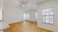 This single-story, one-bedroom, one-bathroom unit is efficiently designed to maximize functionality within a compact footprint. The combined kitchen and living area forms the heart of the space, anchored by soaring vaulted ceilings and a ceiling fan that enhance the sense of openness. Large windows and a glass-panel entry door allow abundant natural light to flood the living area, which features warm-toned wood-look flooring. The kitchen is outfitted with white shaker cabinetry, granite-look countertops, a peninsula with a built-in sink, and a full suite of stainless steel appliances including a refrigerator, range, microwave, and dishwasher. A louvered-door closet adjacent to the kitchen conceals the in-unit laundry area. The bedroom offers plush carpeting, a ceiling fan, built-in shelving, a granite-topped desk nook, and a sliding glass door providing outdoor access. A spacious walk-in closet with dual wire-rack shelving systems serves the bedroom. The bathroom includes a tiled shower-tub combination, a granite-topped vanity, and wood-look flooring, maintaining a clean, cohesive aesthetic throughout the unit.