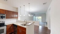 Located at 150 Commons Way in Doylestown, PA, this 2-bedroom, 2-bathroom residence offers a well-designed single-floor layout that maximizes both comfort and functionality. The open-concept living area serves as the heart of the home, seamlessly connecting the kitchen, dining, and living spaces. A tile-surround fireplace anchors the living room, which features plush carpeting and a sliding glass door that fills the space with natural light and provides access to an outdoor balcony. The kitchen is appointed with rich wood cabinetry, granite countertops, a peninsula with a stainless steel sink, pendant lighting, and black stainless appliances, including a range and dishwasher. Both bedrooms are generously proportioned with soft carpet flooring and ample closet space. The primary bedroom benefits from natural light through large windows with views of surrounding greenery. Each of the two bathrooms features a tub-shower combination with a rainfall-style showerhead, a wood-cabinet vanity, and light tile flooring. A hallway connects the private areas of the home, and two dedicated closets offer practical storage solutions. The neutral color palette and clean finishes throughout create a bright, move-in-ready atmosphere.