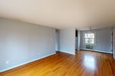 Located at 22 Revere Dr in Bloomfield, CT, this one-bedroom, one-bathroom unit offers a practical and functional layout across a single floor. Warm hardwood flooring runs throughout the living spaces, lending a classic character to the interior. The living room is open and generously proportioned, featuring light gray walls, clean white baseboards, a ceiling fan, and a wall-mounted air conditioning unit beneath a window that invites natural light. A red accent door adds a subtle pop of color to the space. The bedroom is a well-sized retreat, highlighted by a large wall of built-in louvered closet doors that provide ample storage, along with a broad window offering views of the surrounding tree-lined grounds. An additional smaller room with its own window provides flexibility for use as a secondary space or den. The kitchen is equipped with warm wood cabinetry, white countertops, and a double-basin stainless steel sink beneath a window with views of the exterior brick façade. The bathroom includes a full bathtub with white tile surround, a vanity with wood cabinetry, tile flooring, and a window for natural ventilation. Baseboard heating is present throughout the unit, ensuring comfort year-round.