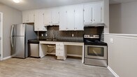 Located at 1100 Ray Suggs Pl NW in Concord, NC, this single-floor, 2-bedroom, 1-bathroom home offers a functional and well-organized layout with consistent neutral tones throughout. The living room features durable wood-look flooring, a ceiling fan with light fixture, and a textured ceiling, creating a comfortable and practical gathering space. A pass-through opening connects the living area to the kitchen, which is outfitted with white cabinetry, dark granite-style countertops, a dark tile backsplash, and stainless steel appliances including a range and dishwasher. Both bedrooms are carpeted for comfort and each includes its own closet with built-in shelving for convenient storage. The primary bedroom is a well-proportioned space featuring a ceiling fan and a window that allows natural light to filter in. The shared full bathroom includes a combination tub and shower with brushed nickel grab bars and fixtures, finished with matching wood-look flooring. Warm beige and taupe wall tones carry throughout the home, contributing to a cohesive and understated aesthetic. White trim and six-panel doors add a clean, classic touch to every room in the home.