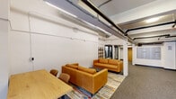 Located at 1110 Washington Ave in downtown St. Louis, this single-floor amenity space offers a well-rounded combination of social and fitness facilities. The layout is anchored by an open lounge area furnished with tan leather sofas arranged over a colorful area rug, complemented by a wooden table and chairs. A freestanding open shelving unit with metal framing and warm wood shelves adds a modern decorative element, while potted greenery introduces a touch of life to the space. Adjacent to the lounge, a wall-mounted mailbox bank and glass-paneled doors provide functional building amenity access.

The fitness center occupies a dedicated area with noticeably elevated ceilings, exposed ductwork, and track lighting. It is equipped with a treadmill, stationary spin bike, a full dumbbell rack, a TRX suspension training station, a weight bench, and a smart interactive mirror for guided workouts. Full-length mirrors line the fitness area walls, enhancing the sense of openness. Large interior windows connect the gym visually to the lounge area, maintaining a sense of connectivity throughout the floor. Neutral-toned carpet tiles, white walls, and industrial-style exposed mechanical systems give the space a clean, modern aesthetic consistent with an urban residential building's amenity offering.