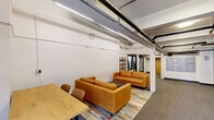 Located at 1110 Washington Ave in downtown St. Louis, this single-floor amenity space offers a well-rounded combination of social and fitness facilities. The layout is anchored by an open lounge area furnished with tan leather sofas arranged over a colorful area rug, complemented by a wooden table and chairs. A freestanding open shelving unit with metal framing and warm wood shelves adds a modern decorative element, while potted greenery introduces a touch of life to the space. Adjacent to the lounge, a wall-mounted mailbox bank and glass-paneled doors provide functional building amenity access.

The fitness center occupies a dedicated area with noticeably elevated ceilings, exposed ductwork, and track lighting. It is equipped with a treadmill, stationary spin bike, a full dumbbell rack, a TRX suspension training station, a weight bench, and a smart interactive mirror for guided workouts. Full-length mirrors line the fitness area walls, enhancing the sense of openness. Large interior windows connect the gym visually to the lounge area, maintaining a sense of connectivity throughout the floor. Neutral-toned carpet tiles, white walls, and industrial-style exposed mechanical systems give the space a clean, modern aesthetic consistent with an urban residential building's amenity offering.