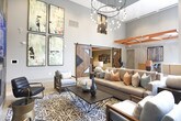 Located at 437 Memorial Drive SE in Atlanta, GA, this thoughtfully designed single-floor amenity space blends contemporary aesthetics with inviting, functional areas. The space is immediately distinguished by its soaring ceilings accented with bold, exposed orange structural beams, lending an industrial-chic character throughout.

The main lounge area serves as the heart of the space, anchored by a dramatic floor-to-ceiling stone tile accent wall housing a sleek linear fireplace and a mounted flat-screen TV. A striking gold metallic wall sculpture crowns the fireplace wall, adding an artistic focal point. Comfortable seating arranged around a patterned area rug creates a warm and welcoming gathering environment.

Adjacent to the lounge, a recessed alcove with brick-textured walls, built-in bench seating with colorful throw pillows, and warm wall sconces offers a more intimate retreat for relaxation or conversation.

A dedicated high-top bar table with barstool seating provides a casual workspace or social hub, positioned beneath the dramatic beamed ceiling with views to an outdoor courtyard through floor-to-ceiling glass doors and windows. A decorative rustic barn door adds a charming design contrast. Large-format tile flooring runs consistently throughout, anchoring the space with a clean, cohesive look. Curated artwork displayed throughout reinforces the creative, community-centered atmosphere.