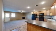 This single-floor home offers a practical and well-organized layout designed for comfortable everyday living. The open-concept kitchen and living area serves as the heart of the home, where light maple cabinetry, dark countertops, and a full suite of black appliances — including a refrigerator, range, microwave, and dishwasher — define a functional kitchen space. A peninsula counter provides additional workspace and separates the kitchen from the living area, which features plush carpeting, a ceiling fan, and a fireplace. Tile-style flooring flows through the kitchen and connects to the entryway, which includes a windowed exterior door that brings in natural light. The bedrooms are generously sized with neutral-toned walls, carpeted floors, and baseboard heating. One bedroom includes access to a spacious walk-in closet outfitted with wire shelving and hanging rods. The bathroom is well-appointed with a wood-toned vanity, dark countertop, a stand-up shower, and stone-look tile flooring. A dedicated laundry room with full-size washer and dryer hookups and overhead wire shelving adds everyday convenience. Throughout, warm wood trim accents and muted wall tones contribute to a cohesive, understated aesthetic.