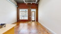 Located at 316 King St in Greensboro, NC, this urban loft showcases a striking industrial aesthetic throughout. Soaring ceilings with exposed steel trusses, visible ductwork, and track lighting define the open-concept main living area, creating a spacious, warehouse-inspired atmosphere. Polished concrete floors with warm amber tones run consistently throughout the unit, adding character and visual continuity.

The combined living, dining, and kitchen area serves as the heart of the loft. The well-appointed kitchen features light maple cabinetry, granite-style countertops, a central butcher-block island, stainless steel appliances including a gas range with a stainless steel hood, and a built-in dishwasher. An exposed brick wall with large windows and a glass-paned entry door floods the living area with natural light and adds authentic industrial charm.

The bedroom is generously sized, offering ample space for furnishings, and includes two closets with built-in hanging rods for convenient storage. The loft also includes a full bathroom. The minimalist, neutral wall palette complements the raw architectural elements, making this space ideal for those who appreciate urban, loft-style living in the heart of Greensboro.