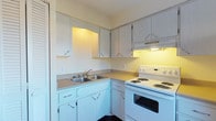 This single-floor residence offers a thoughtfully arranged two-bedroom, one-bathroom layout designed for comfortable everyday living. The kitchen is a functional highlight of the home, featuring an L-shaped configuration with ample white cabinetry that extends to the upper and lower sections of the walls, providing generous storage throughout. A double-basin sink sits beneath under-cabinet lighting, complementing the coil electric range and oven finished in white. The countertops offer a practical workspace suitable for meal preparation, and an open pass-through adds a sense of connectivity between the kitchen and the adjoining living area. The cabinetry hardware and neutral color palette give the kitchen a clean, understated aesthetic. The overall layout of the residence is efficient and accessible, making good use of the available floor space across a single level. The two bedrooms provide private retreats, while the shared bathroom serves the household conveniently. The straightforward design and functional finishes throughout make this a practical and move-in ready living space well-suited for a range of residents.
