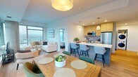 This well-appointed two-bedroom, two-bathroom unit in Calgary, AB offers a thoughtfully designed open-concept layout with light hardwood flooring flowing throughout the space. The living area is a standout, featuring expansive floor-to-ceiling windows and access to a balcony, flooding the room with natural light and framing sweeping panoramic views of the Calgary cityscape. A distinctive exposed concrete column adds an industrial-modern touch to the living space.

The kitchen is both functional and stylish, outfitted with light wood cabinetry, a subway tile backsplash, stainless steel appliances, and a generous waterfall-edge island with bar seating and pendant lighting. The adjacent dining area benefits from its own large corner window, offering additional city views and a bright setting for meals.

The hallway connecting the bedrooms features clean white walls and recessed lighting, lending a calm, gallery-like feel. Both bedrooms are comfortably scaled, with light-filled interiors and ample closet storage. The primary bedroom includes a walk-in closet. The two bathrooms are finished in crisp white tile, with one featuring a full soaker tub and large-format subway tile surround. The overall aesthetic is clean, contemporary, and cohesive.