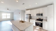 Located at Jefferson Ridge Drive in Jeffersonville, Indiana, this well-appointed two-bedroom, two-bathroom residence offers a thoughtfully designed single-level layout. The open-concept kitchen is a standout feature, showcasing granite countertops, crisp white shaker cabinetry, stainless steel appliances including a refrigerator, range, and microwave, and a central island with a built-in sink — ideal for both cooking and entertaining. The living room benefits from vaulted ceilings, a ceiling fan, and large windows that invite generous natural light and outdoor views, complemented by durable hardwood-style flooring throughout the main living areas. The spacious primary bedroom features vaulted ceilings, multiple windows offering bright natural light, and plush carpeting. The second bedroom is equally well-lit, with wide windows and soft carpet flooring. Both bathrooms are finished with granite-topped white vanities and full tub/shower combinations with brushed nickel hardware. Three closets provide ample storage throughout the unit. A dedicated laundry room with a full-size washer and dryer adds everyday convenience. The overall palette of soft gray walls and light finishes gives the entire space a clean, modern, and welcoming ambiance.
