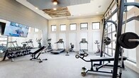 Located in Midlothian, Texas, this fitness center offers a thoughtfully designed workout space spread across a single open floor. The room makes a strong architectural impression with soaring walls, a row of clerestory windows that line the upper perimeter, and a distinctive reclaimed wood ceiling accent panel that adds a rustic, modern touch above the main exercise area. A large glass garage-style door on one wall floods the space with natural light and provides open views of the surrounding community.

The interior features durable speckled rubber flooring throughout, ideal for high-impact activity. Full-length mirrors are strategically positioned along one wall to maximize the sense of space and support proper form during workouts. Cardio equipment is well-represented, with multiple treadmills, ellipticals, a stationary bike, and a rowing machine arranged along the windowed wall. A multi-function cable machine anchors the strength training area, complemented by a rack of dumbbells, medicine balls, stability balls, and adjustable benches for versatile training options. A large flat-screen television is mounted prominently, providing an engaging visual focal point. Shiplap-style wall paneling and a ceiling fan complete the polished yet functional aesthetic of this community fitness facility.