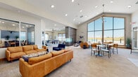Located on E Philadelphia Street in Rapid City, South Dakota, this single-story community clubhouse delivers a thoughtfully designed gathering space with a contemporary aesthetic rooted in regional character. The open-plan layout is anchored by soaring ceilings and a dramatic floor-to-ceiling window wall that floods the interior with natural light and frames sweeping outdoor views of the surrounding landscape.

At the heart of the space stands a striking double-sided fireplace clad in dark metal with an etched reed motif, serving as both a functional focal point and a visual divider between the lounge and game areas. The lounge features warm cognac leather sofas, a cowhide rug, and eclectic Western-inspired artwork, creating an inviting, relaxed atmosphere. Nearby, café-style dining tables with light wood and metal chairs provide casual seating throughout.

A well-appointed kitchenette with warm wood cabinetry, quartz countertops, and a coffee station supports the social areas. The game zone includes a foosball table and additional recreational options. A dedicated conference room accommodates collaborative meetings, equipped with a large display screen, a wood conference table, and ample seating. Recessed lighting and ceiling fans complete the comfortable, polished interior throughout.