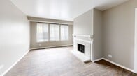This single-story, 2-bedroom, 2-bathroom residence offers a well-organized layout across a comfortable footprint. The living room serves as the focal point of the home, featuring a white-painted brick fireplace with a classic mantel and a large multi-pane window that invites abundant natural light. Light hardwood-style flooring runs throughout the main living areas, lending a cohesive and clean aesthetic.

A dedicated dining area adjoins the kitchen, featuring wood-look flooring and a bright window with horizontal blinds. The kitchen is equipped with white cabinetry. A sliding glass door in the living space provides direct outdoor access and is fitted with vertical blinds for light control. A ceiling fan with a light fixture adds functionality to the space.

The two bedrooms are carpeted and well-proportioned. The primary bedroom includes a closet and wall sconce lighting, while both rooms feature windows with blinds for natural light. Connecting hallways provide a logical flow between the bedrooms and bathrooms.

Both bathrooms include a white vanity with a single sink, mirror, and a glass-door shower enclosure with brushed nickel hardware and wood-look tile flooring. Neutral gray-toned walls are consistent throughout, creating a calm and understated ambiance.