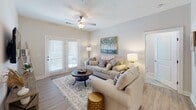 Located in Greenville, NC, this single-floor residence on Dunhagan Road offers a thoughtfully designed open-concept layout with modern finishes throughout. The kitchen serves as a central hub of the space, showcasing rich dark cabinetry, light granite countertops with a subway tile backsplash, a peninsula island with pendant lighting overhead, and a full suite of stainless steel appliances including a French door refrigerator, electric range, microwave, and dishwasher. Light wood-style flooring flows seamlessly from the kitchen through the dining and living areas, creating a cohesive and airy feel. The living room is generously sized, filled with natural light from French doors that open to an outdoor area, and features a ceiling fan for added comfort. Two bedrooms provide comfortable retreats, each with plush carpet flooring, ceiling fans, and ample natural light from well-positioned windows. The primary bedroom includes access to a walk-in closet. The bathroom is finished with dark wood cabinetry, granite countertops, tile flooring, and a shower/tub combination. Neutral tones and clean architectural lines give the entire space a bright, welcoming ambiance suited for everyday living.