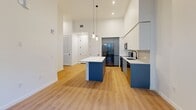 Located at 501 NW Seventh Terrace in Fort Lauderdale, FL, this modern one-bedroom, one-bathroom residence offers a thoughtfully designed open-concept layout with impressive soaring ceilings throughout. Light wood-tone flooring flows seamlessly across the living, dining, and kitchen areas, creating a bright and cohesive aesthetic.

The kitchen is a standout feature, showcasing two-tone cabinetry with crisp white upper cabinets and bold blue lower cabinets, complemented by a white quartz countertop, subway tile backsplash, and stainless steel appliances including a refrigerator, range, and microwave. A central island provides additional prep and seating space, while modern cylindrical pendant lights add a contemporary finishing touch. Large floor-to-ceiling windows and a glass door lead to a private balcony, framing lush tropical palm views and filling the space with abundant natural light.

The spacious bedroom continues the clean, airy design with direct balcony access and generous closet space, including a walk-in closet with built-in wire shelving. The bathroom features large-format tile flooring, a walk-in glass shower with floor-to-ceiling tile surround, a floating vanity with white quartz countertop, and matte black fixtures throughout. Additional conveniences include a dedicated laundry area and ample hallway closets.