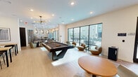 Located on Cumberland Avenue in Knoxville, Tennessee, this generously sized single-floor community amenity space offers a well-rounded social and recreational environment. The open layout is anchored by light wood-look tile flooring and recessed lighting throughout, creating a bright and modern atmosphere.

A central game area features a full-size pool table, complemented by contemporary rounded lounge chairs and compact side tables — ideal for casual gatherings. Large floor-to-ceiling windows and glass doors line one wall, flooding the space with natural light and providing direct views of and access to an outdoor patio and pool area.

A dedicated media lounge offers a cozy retreat, highlighted by a dramatic stone-patterned accent wall lined with open shelving and dual flat-screen televisions, perfect for watching sports or entertainment. Warm leather seating and eclectic pendant lighting give this zone a distinct, inviting character.

Throughout the space, multiple flexible seating arrangements — including bar-height tables, round bistro tables, and soft modular lounge pieces — accommodate both social interaction and quiet relaxation. A separate, more intimate sitting area with a sectional sofa and framed windows rounds out the offerings. The overall design blends contemporary aesthetics with functional versatility, making this a standout communal destination.