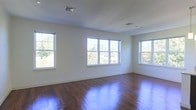 This single-floor space presents a clean and open interior characterized by rich, dark hardwood flooring that extends throughout the room, reflecting abundant natural light. Three generously sized windows line the walls, drawing in daylight from multiple angles and providing views of surrounding greenery, contributing to an airy and welcoming atmosphere. The walls are finished in a crisp white, enhancing the sense of brightness and openness within the space. Ceiling-mounted HVAC vents are integrated discreetly into the white ceiling, indicating a central air system. The neutral color palette and minimal architectural detailing create a versatile backdrop well-suited for a variety of uses. The hardwood floors are in polished condition, adding warmth and a sense of quality to the overall aesthetic. With its combination of natural light, durable flooring, and open layout, this space offers a functional and adaptable environment that can accommodate a range of configurations and purposes.