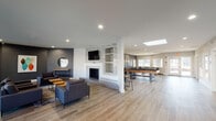 The Trails of Sunbrook Clubhouse in Saint Charles, Missouri, is a thoughtfully designed single-story community facility that offers residents a variety of amenities within a contemporary, open layout. Light wood-look flooring flows throughout the space, complementing a neutral palette of white and charcoal-gray walls that give the clubhouse a modern, polished aesthetic.

The central lounge area is a standout feature, anchored by a striking floor-to-ceiling mosaic tile fireplace surround with built-in shelving and a mounted flat-screen television. Comfortable sectional seating and accent tables create an inviting gathering space, enhanced by recessed lighting and a skylight that introduces natural light from above. Colorful artwork adds personality to the lounge's dark-toned walls.

Adjacent to the lounge, a dedicated game room provides recreational options including a billiards table and foosball table, with a wall-mounted TV and seating for spectators. Large windows along the entry area flood the space with natural light and offer views of the outdoor surroundings, with direct access to an exterior patio.

A fitness area is also accessible from the main lounge, equipped with exercise equipment and mirrored walls to support residents' wellness routines. The clubhouse additionally includes a well-appointed, ADA-accessible restroom featuring a floating stone-topped vanity, elegant vanity lighting, and wood-look flooring.