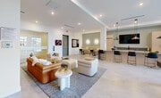 Located at 27077 S Dixie Hwy in Homestead, FL, this single-floor community space offers a generously sized, open-plan layout designed with a clean, contemporary aesthetic. The interior is defined by crisp white walls, smooth light-toned tile flooring, and recessed lighting throughout, creating a bright and welcoming atmosphere that is further enhanced by large glass-panel doors and windows that invite abundant natural light from the outdoors.

The main living area serves as the social centerpiece, featuring a curated arrangement of modern lounge seating — including a rich cognac leather sofa, plush neutral armchairs, and sculptural accent tables — all anchored by a textured area rug. Structural columns are integrated seamlessly into the design, adding architectural character without interrupting the open flow of the space.

A dedicated billiards zone with a full-size pool table and vibrant wall art adds a recreational dimension to the layout. Adjacent to the main lounge, a cozy built-in banquette nook with soft wall sconces and marble-top tables provides an intimate setting for casual gatherings or tabletop games. A bar-height counter with seating and a wall-mounted television rounds out the amenities. Lush indoor plants are placed throughout, adding warmth and a touch of greenery that complements the modern, airy design.