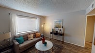 This single-floor residential unit offers a functional and comfortable layout across several well-defined living spaces. The living room serves as the heart of the home, featuring wood-look flooring, a textured ceiling, and a large window with blinds and sheer curtains that allow natural light to fill the room. The space comfortably accommodates a seating area and provides a welcoming atmosphere.

The kitchen is outfitted with crisp white shaker-style cabinetry, a stainless steel sink, white countertops, and black appliances including a refrigerator and dishwasher. Ample upper and lower cabinet storage makes the kitchen highly practical for everyday use.

The unit includes two bedrooms, each finished with soft carpet flooring and equipped with ceiling fans for year-round comfort. The primary bedroom features warm-toned curtains, a window with blinds, and good natural light. The secondary bedroom includes a sliding closet and an additional window for ventilation and brightness.

A shared hallway connects the main living areas to the bedrooms and bathroom. The bathroom features a white vanity with a single sink, clean white cabinetry below, and a well-lit mirror. Wood-look flooring continues through the hallway, maintaining a cohesive aesthetic throughout the unit. Overall, the space is practical, neatly designed, and move-in ready.