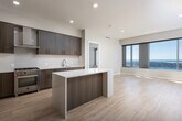 This single-floor residence showcases a contemporary design with light hardwood flooring and a neutral palette carried consistently throughout. The open-concept kitchen serves as a central highlight, featuring dark wood-grain cabinetry extending to the ceiling, light quartz countertops, a clean tile backsplash, and a stainless steel range with a professional-grade gas cooktop beneath a wall-mounted hood. A built-in wine refrigerator is integrated into the kitchen island, adding a refined touch. A stainless steel refrigerator completes the suite of appliances.

The living area benefits from floor-to-ceiling windows that frame striking panoramic water views, flooding the space with natural light. The bedroom continues this theme, offering expansive window views of the waterway and surrounding landscape. Adjacent to the bedroom, a walk-in closet provides built-in shelving and hanging systems finished in dark wood.

The bathroom is well-appointed with a wide floating vanity, dual integrated sinks, a large backlit mirror, and a glass-enclosed shower with tile surround. A dedicated laundry room houses a full-size side-by-side washer and dryer with overhead shelving for added storage convenience.