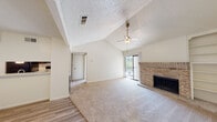 This single-floor residence offers a well-organized layout that balances open communal spaces with comfortable private areas. The living room serves as the focal point of the home, showcasing soaring vaulted ceilings accented by a textured finish, a ceiling fan with light fixture, and a full-height brick fireplace that anchors the space with warmth and character. Sliding glass doors lead to a private balcony, filling the room with natural light and offering views of the surrounding greenery. Plush carpeting throughout the living and bedroom areas adds a layer of comfort underfoot, while wood-look vinyl flooring transitions seamlessly into the kitchen and entryway. The kitchen is efficiently designed with dark cabinetry, light countertops, and black appliances including a refrigerator, electric range, and built-in microwave, all complemented by a sink and dishwasher along the opposing wall. The bedroom is generously proportioned, featuring a ceiling fan, mirrored closet doors, and direct access to the bathroom. The bathroom includes a tiled shower-tub combination, a window for natural ventilation, wood-look flooring, and a vanity with dark cabinetry. The entryway benefits from vaulted ceilings as well, creating an airy and welcoming introduction to the home.