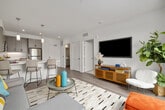 This well-appointed one-bedroom, one-bathroom residence combines modern design with functional living across a single floor. The open-concept kitchen and living area serves as the heart of the home, featuring a sleek kitchen island with a white quartz countertop and seating for multiple bar stools, pendant lighting, gray cabinetry, stainless steel appliances — including a refrigerator, range, and microwave — and wood-look flooring that flows throughout the main living areas. The living room is bright and airy, benefiting from large sliding glass doors that open onto a private balcony offering sweeping outdoor views, ideal for relaxing or entertaining. The bedroom is a comfortable, carpeted retreat with a window that brings in natural light and scenic views, complemented by access to a dedicated walk-in closet with built-in shelving and hanging rods. The full bathroom features a tub-shower combination with wood-look tile flooring and clean, neutral finishes. Throughout the residence, crisp white walls, modern fixtures, and thoughtful design details create a cohesive, contemporary atmosphere that is both inviting and practical.