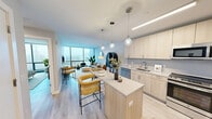 Located at 325 Huguenot St in New Rochelle, NY, this thoughtfully designed one-bedroom, one-bathroom residence offers a seamless open-concept layout with well-appointed finishes throughout. Light wood flooring flows across the entire space, creating a warm and cohesive aesthetic.

The kitchen is a standout feature, outfitted with light wood cabinetry, stainless steel appliances, a built-in island with seating, and pendant lighting. It opens directly into the living and dining areas, making the space ideal for both daily living and entertaining. The living room is anchored by expansive floor-to-ceiling windows that flood the area with natural light and offer open city views.

The generously sized primary bedroom continues the light, airy palette with soft blue-gray walls, light wood flooring, and its own floor-to-ceiling window with a built-in bench seat, framing elevated views of the surrounding cityscape.

The bathroom is finished with large-format stone-look tile, a glass-enclosed walk-in shower with full-height tile surround, and a light wood vanity with a white countertop and illuminated mirror, delivering a clean, spa-like feel.

Overall, this residence combines modern design with an abundance of natural light and urban views.