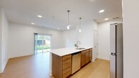 This thoughtfully designed single-floor residence in Blair, Nebraska offers a clean, contemporary aesthetic throughout its well-organized layout. The open-concept kitchen serves as a central highlight, featuring warm wood cabinetry, stainless steel appliances including a full-size refrigerator, microwave, and range, and a spacious peninsula with a white countertop and integrated sink. Pendant lighting above the peninsula adds a modern touch, while light wood-style flooring runs through the main living and kitchen areas, enhancing the bright, airy atmosphere created by white walls and recessed lighting. The living area extends to the outdoors via sliding glass doors, offering views of the surrounding landscape and direct access to a patio. The bedroom is a comfortable, carpeted retreat featuring a ceiling fan, a window with outdoor views, and ample natural light. The bathroom is finished with warm wood cabinetry, a white countertop vanity, a large mirror, and a grab bar, reflecting both style and practicality. Throughout the space, clean lines, neutral tones, and quality finishes create a cohesive and inviting environment suitable for everyday living.