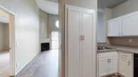 Located at 23639 Newhall Ave in Santa Clarita, California, this single-floor residence offers a well-designed layout with a blend of modern finishes and functional living spaces. The living area is a standout, featuring dramatically vaulted ceilings with a distinctive circular porthole window that draws in natural light, and a sleek black fireplace anchoring the room. Sliding glass doors with vertical blinds open to an outdoor area, providing views of surrounding greenery and filling the space with abundant natural light. Wood-style plank flooring runs throughout the main living and kitchen areas, lending a clean, cohesive aesthetic. The kitchen is thoughtfully appointed with crisp white cabinetry, granite-style countertops, a full suite of black appliances including a refrigerator, range, built-in microwave, and dishwasher, as well as a tall pantry cabinet for generous storage. The bedrooms feature plush carpeting and large windows that invite natural light, with closet access conveniently integrated. The bathroom includes a white vanity with a granite-style countertop, a large mirror, and a shower-tub combination. The open-concept flow between the kitchen and living areas adds to the sense of spaciousness throughout this well-maintained home.