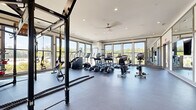 Located on Watervista Terrace in Pooler, Georgia, this generously sized single-floor fitness center offers a comprehensive workout environment designed with both functionality and aesthetics in mind. The space is defined by its expansive, open layout with durable rubber flooring throughout, providing ample room for a wide variety of exercise activities.

Large, floor-to-ceiling windows line multiple walls, flooding the interior with natural light and offering views of the surrounding greenery and neighborhood. A ceiling fan and recessed lighting complement the bright, airy atmosphere. The main workout area houses a full suite of cardio equipment, including treadmills, ellipticals, stair climbers, and stationary bikes from quality brands such as TRUE Fitness.

A dedicated strength training zone features a multi-rack dumbbell station with a broad weight range, a weight bench, plate-loaded machines, and a TRX suspension system with battle ropes for functional training. Full-length mirrors and a decorative accent wall panel enhance the strength area's visual appeal.

Glass-paneled interior walls and double doors connect to an adjacent room, adding transparency and a sense of additional space. The overall ambiance is clean, modern, and well-organized, creating an inviting environment suited for a comprehensive fitness routine.