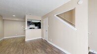 This two-story, one-bedroom, one-bathroom unit in Austin, TX is thoughtfully laid out across two floors. The main level features an open-concept living room with warm wood-style flooring, neutral beige walls, and a textured ceiling. A staircase leads to the upper level, while a pass-through peninsula seamlessly connects the living area to the kitchen. The kitchen is well-appointed with dark espresso cabinetry, granite countertops, a breakfast bar with sink, black appliances including a refrigerator and range, and a skylight that brings in natural light. The upper floor is dedicated to the generously sized bedroom, which is carpeted for comfort and includes a window that allows for natural light. The bedroom provides direct access to both a walk-in closet outfitted with built-in shelving and hanging rods, and the full bathroom. The bathroom features a dark wood vanity with granite countertop, a tiled tub-shower combo, and wood-style flooring. Throughout the unit, the consistent use of neutral tones and quality finishes creates a cohesive and practical living environment well-suited for Austin's vibrant lifestyle.
