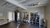 This fitness space at 5802 University in San Diego is designed to support a full range of workout routines. The room features exposed beam ceilings painted white, lending a clean, structured aesthetic to the space. Rubber flooring throughout provides durability and traction underfoot, making it well-suited for high-intensity training. Adjustable track lighting mounted to the ceiling ensures the space is well-lit during use.

The facility is outfitted with a cable resistance machine, an adjustable weight bench, and a stability ball, catering to both functional and strength-based training. A well-stocked dumbbell rack lines one wall, offering a wide range of free weights for varied exercise options. Large mirrors are positioned along one side of the room, expanding the sense of space and allowing users to monitor their form during workouts.

Natural light filters in through windows fitted with blinds, while a glass door provides additional brightness and access. The overall layout is practical and organized, maximizing the use of available floor space while keeping equipment accessible and the environment open and functional.