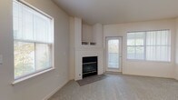 This two-story residence is designed with a clean, neutral aesthetic, featuring light beige walls, plush carpeting, and tile flooring in key areas. The main living area is a standout space, anchored by a fireplace with a tiled hearth and built-in shelving above. Large windows fitted with blinds flood the room with natural light, while a glass-paneled exterior door provides direct outdoor access and additional brightness.

The kitchen is efficiently laid out with light wood cabinetry, white countertops, and tile flooring. It is equipped with a gas range, over-the-range microwave, double basin sink, and a dishwasher, with ample upper and lower cabinet storage throughout.

The residence includes multiple bathrooms across both floors. A half bath on one level features a single vanity with a large mirror and tile flooring. The full bathrooms offer extended vanity countertops with light wood cabinetry, large mirrors, and a shower-tub combination enclosed by sliding glass doors.

The upper floor, accessed via a staircase with a wood handrail, hosts carpeted bedroom spaces. Each bedroom is well-proportioned, featuring sliding closet doors and generously sized windows that bring in natural views and light, contributing to an open, airy atmosphere throughout the home.