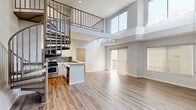 This thoughtfully designed two-bedroom, two-bathroom home spans two floors, offering a generous and functional layout. The main level immediately impresses with soaring double-height ceilings that flood the open living area with natural light through expansive clerestory windows. Light-toned hardwood-style flooring runs throughout, complementing the clean, modern aesthetic. A distinctive spiral staircase adds an architectural focal point while connecting the two levels seamlessly.

The open-concept kitchen is well-appointed with white shaker cabinetry, light quartz countertops, a mosaic tile backsplash, stainless steel appliances including a gas range, built-in microwave, and a French door refrigerator, along with a deep double-basin sink. A peninsula counter provides additional workspace and defines the kitchen's boundary with the living area.

Both bathrooms feature full tub-and-shower combinations finished with floor-to-ceiling large-format gray marble-look tile and brushed nickel fixtures, creating a clean and refined feel. The bedrooms are comfortably sized, each featuring wood-style flooring, neutral gray walls, and windows with roller shades. The primary bedroom includes a built-in closet with mirrored sliding doors and organized shelving. The upper floor provides a more intimate retreat, while the expansive main level offers ample room for living and entertaining.